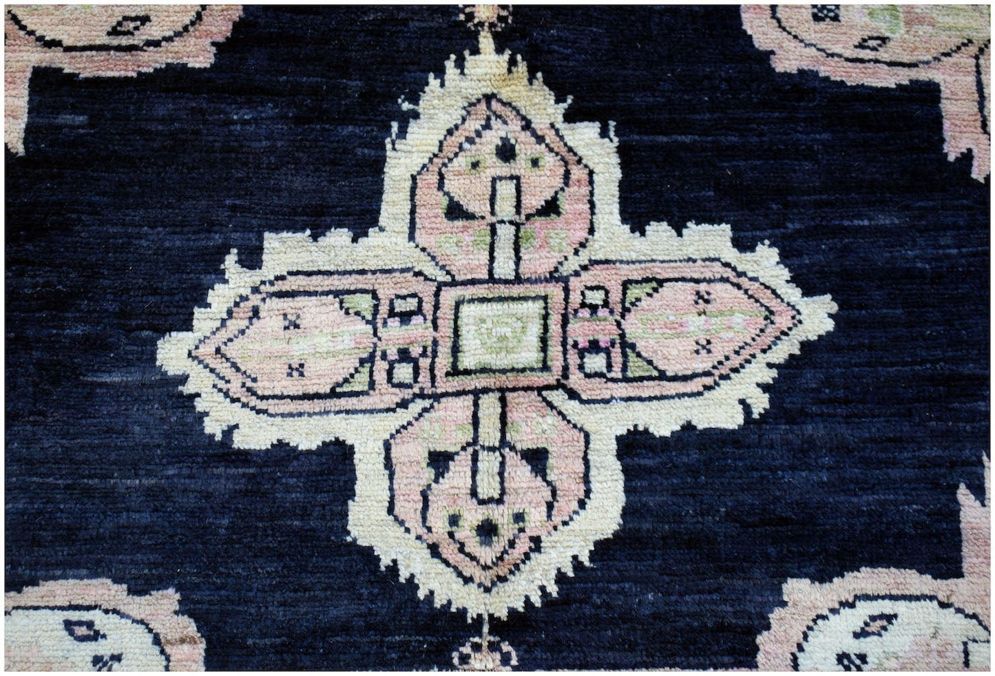 A handmade wool rug featuring a central pink and cream geometric medallion on a dark blue field.