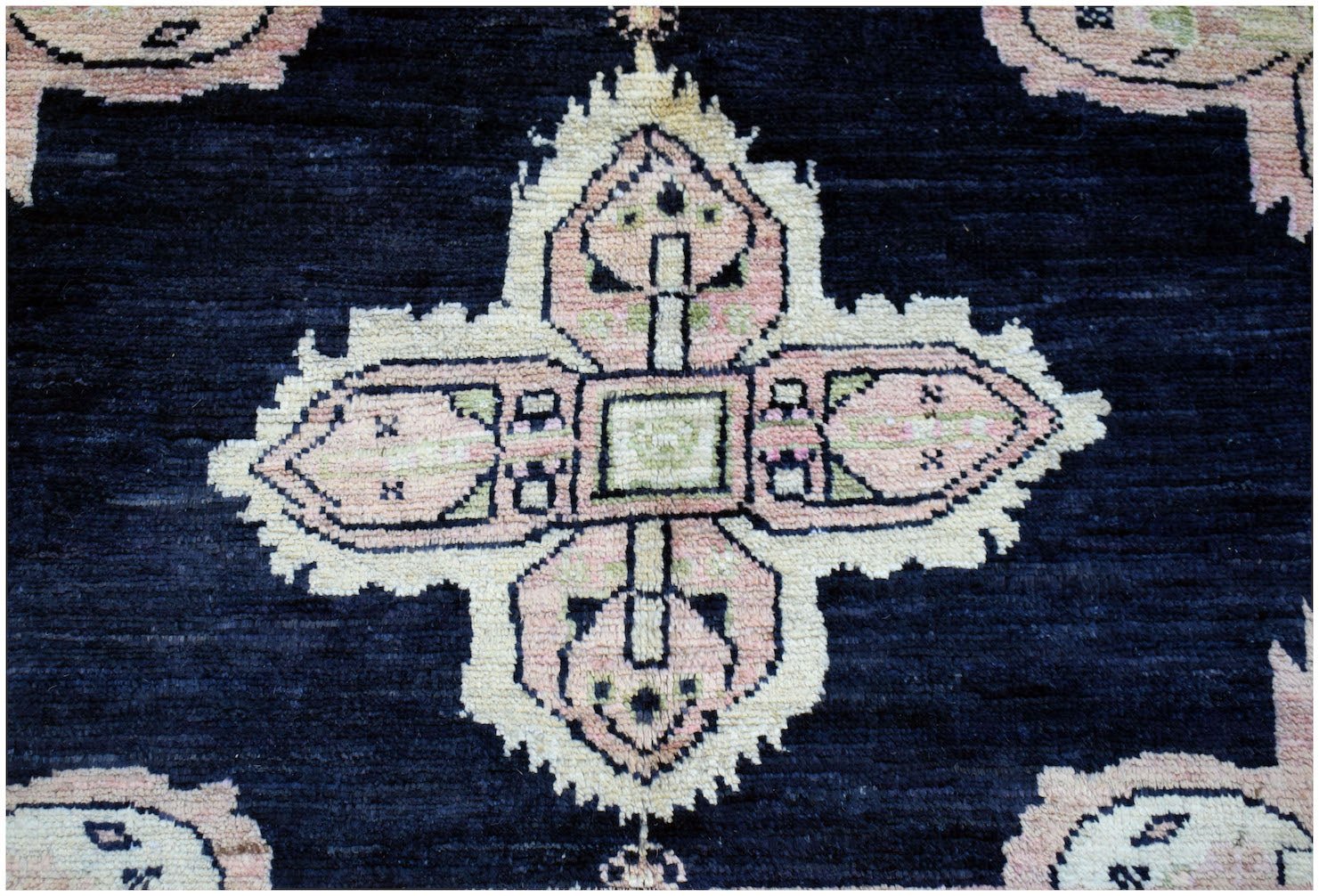 A handmade wool rug featuring a central pink and cream geometric medallion on a dark blue field.
