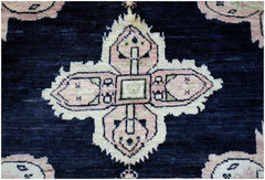 A handmade wool rug featuring a central pink and cream geometric medallion on a dark blue field.
