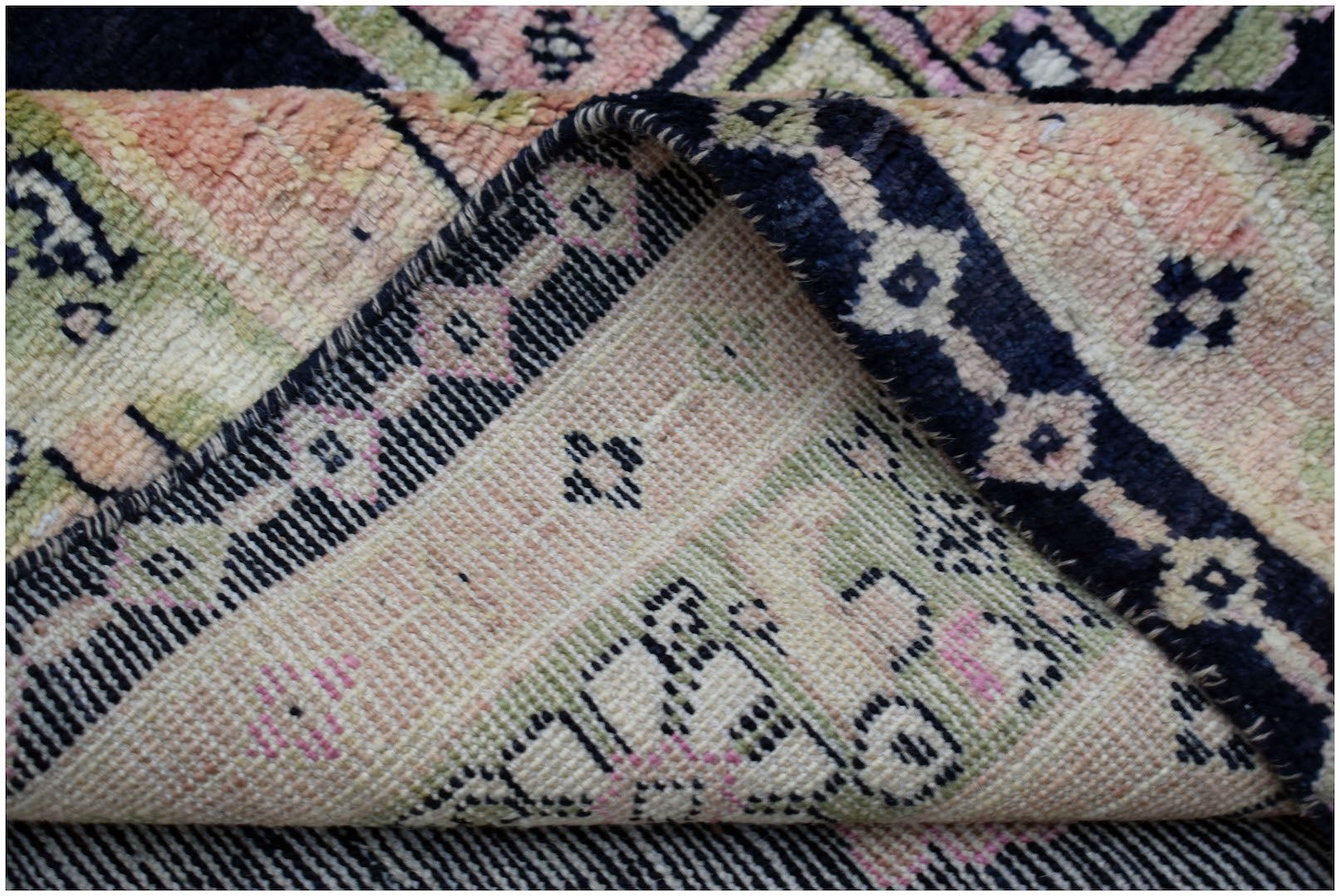 A folded handmade wool rug featuring a geometric pattern in shades of pink, green, and navy blue.