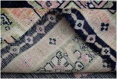 A folded handmade wool rug featuring a geometric pattern in shades of pink, green, and navy blue.