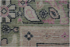 A close-up of a handmade wool rug featuring geometric patterns in green, pink, and cream tones.