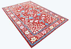 A handmade red wool rug from Afghanistan featuring a floral pattern and a blue border.