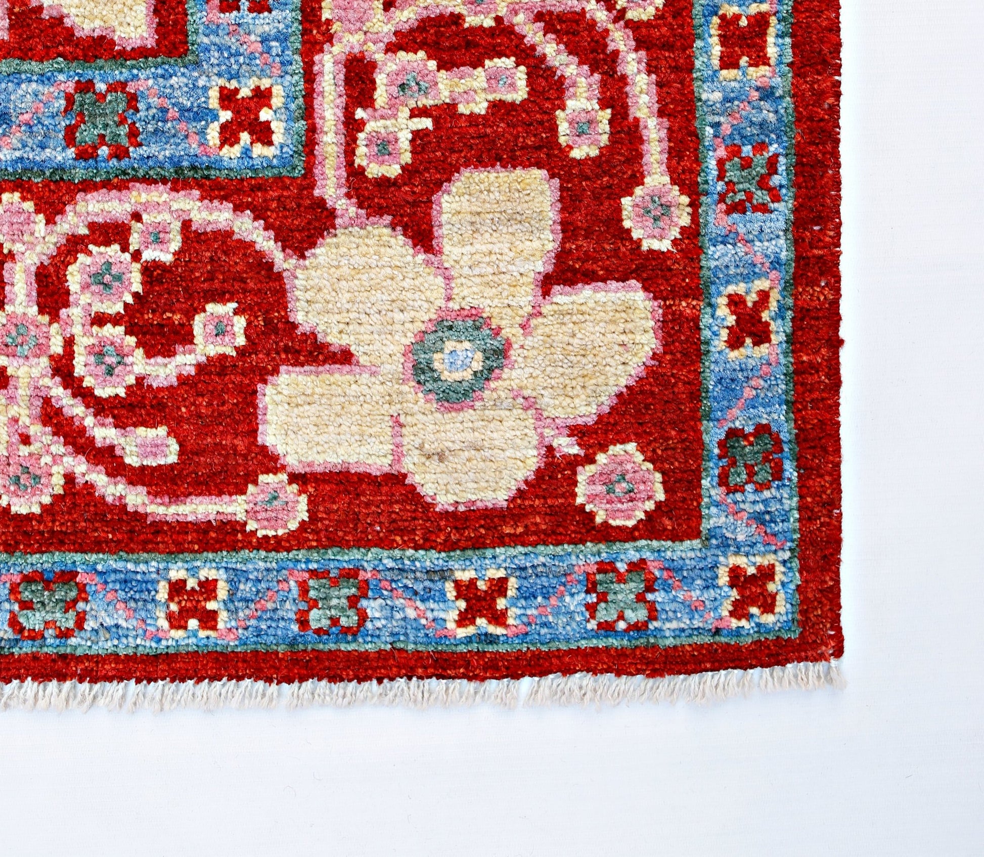 A handmade wool rug featuring a large cream floral motif on a red field with a blue border.