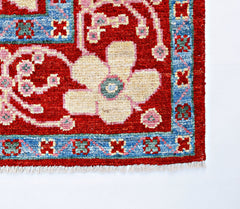A handmade wool rug featuring a large cream floral motif on a red field with a blue border.