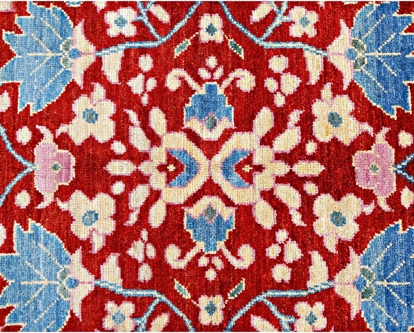 A handmade wool rug from Afghanistan featuring a symmetrical floral pattern in red, blue, and cream.