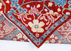 A handmade wool rug from Afghanistan featuring a red field with blue and cream floral patterns.