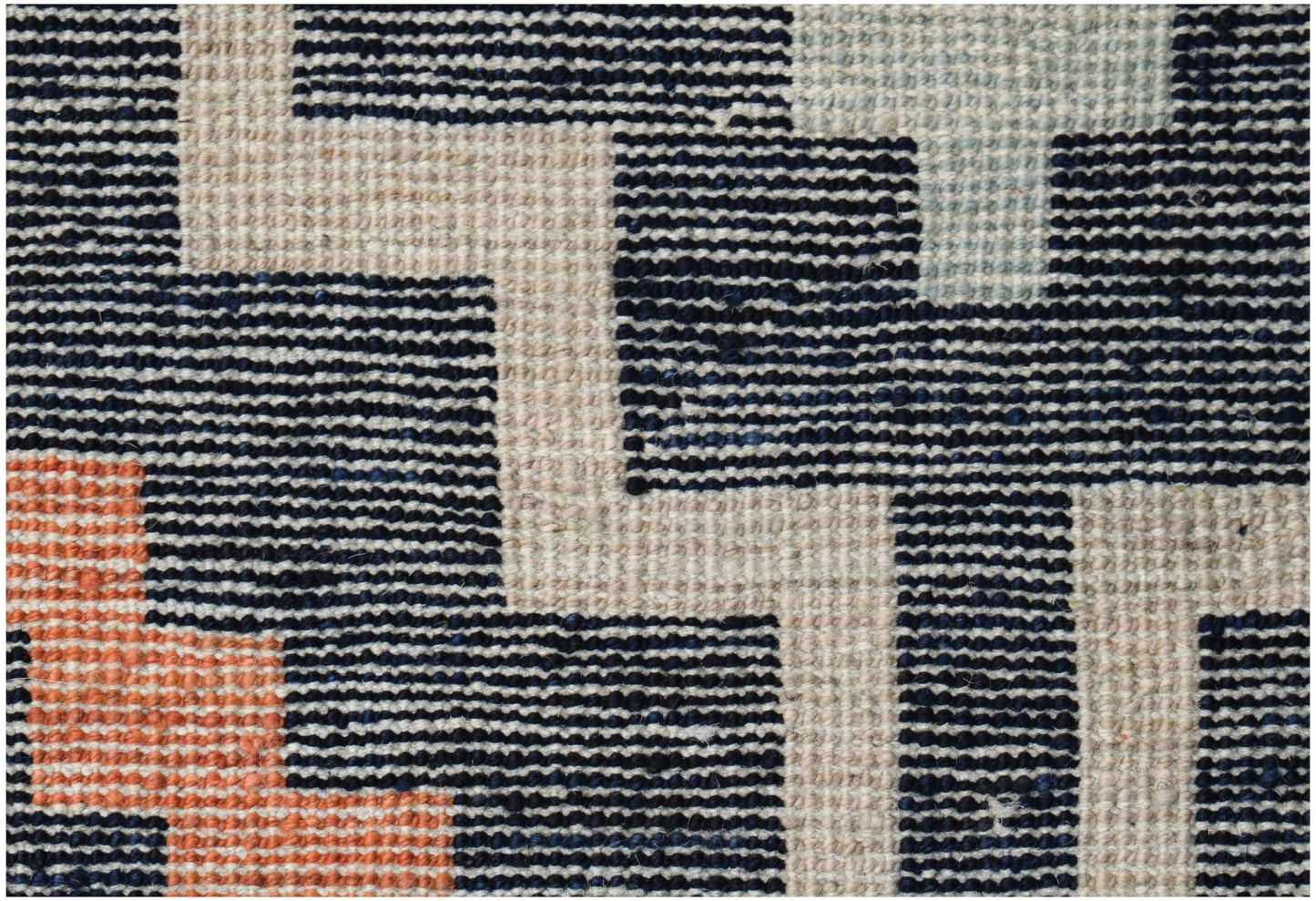A handknotted wool rug featuring a geometric pattern in navy, cream, and orange tones.