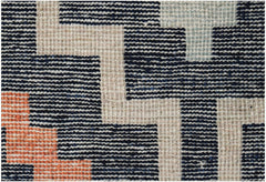 A handknotted wool rug featuring a geometric pattern in navy, cream, and orange tones.