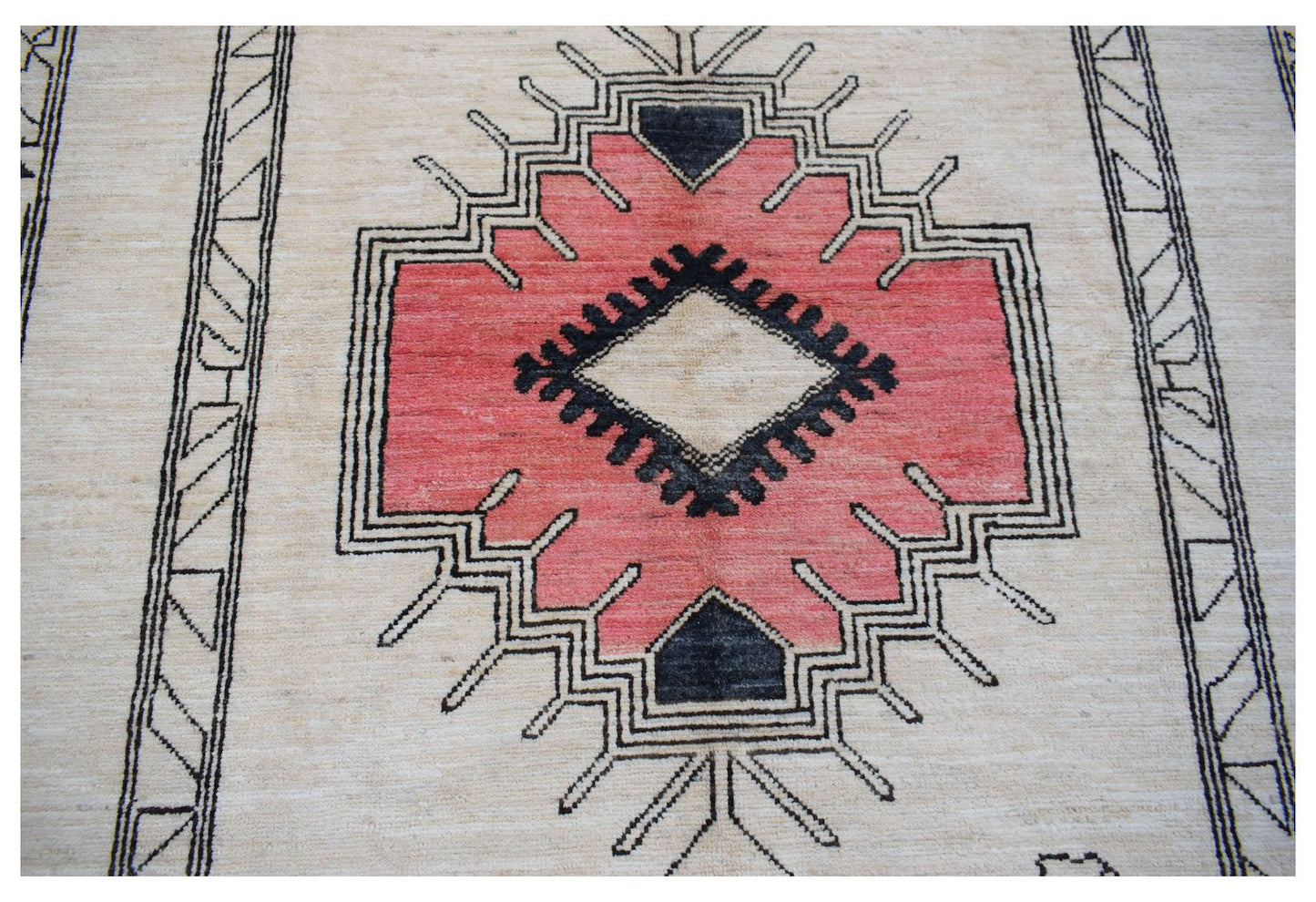 A handmade wool rug featuring a central pink geometric medallion with black accents on a cream base.