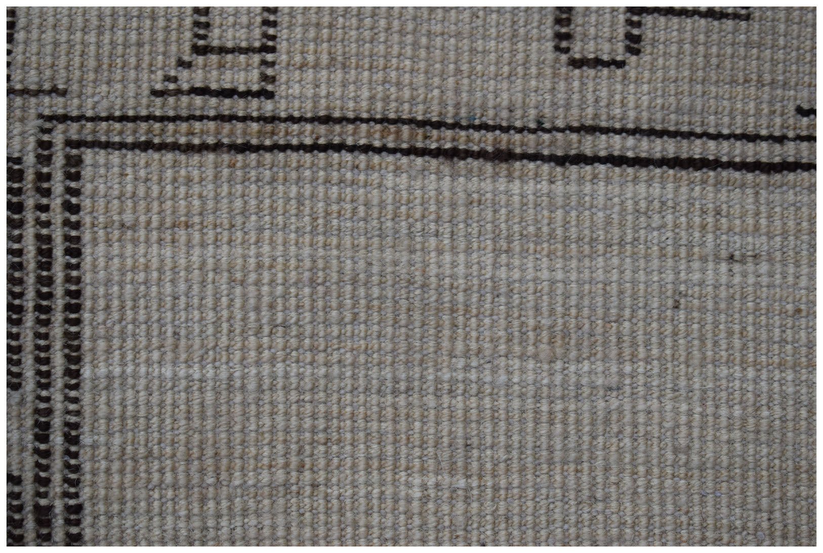 A close-up of a handmade wool rug featuring a neutral beige field with dark brown geometric borders.