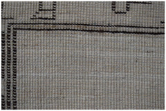 A close-up of a handmade wool rug featuring a neutral beige field with dark brown geometric borders.