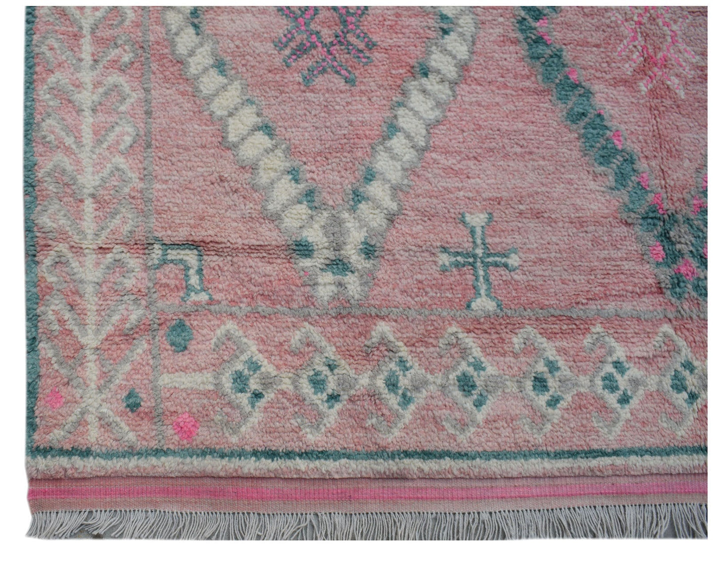 A handmade wool rug featuring a pink background with teal and white geometric tribal patterns.