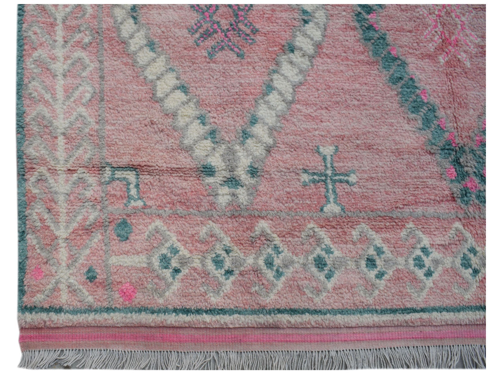 A handmade wool rug featuring a pink background with teal and white geometric tribal patterns.