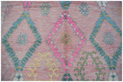 A handmade wool rug featuring a pink background with a repeating diamond pattern in blue and pink.