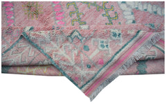 A handmade transitional wool rug in pink with colorful tribal patterns and fringed edges.