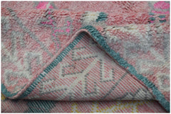A close-up of a plush, handmade wool rug in shades of pink, white, and teal with a folded corner.