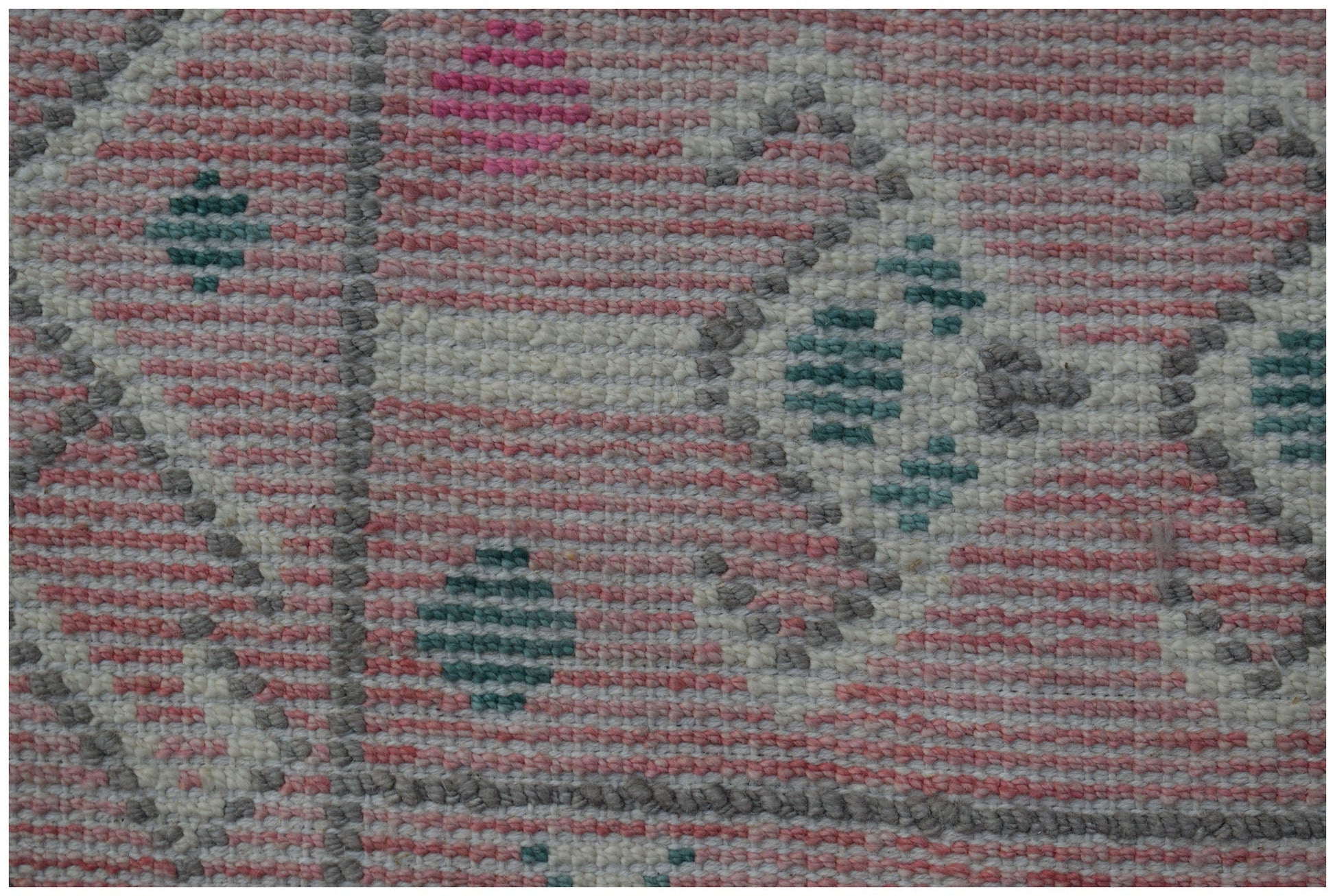 A close-up of a handmade wool rug featuring a pink, white, and teal geometric tribal pattern.