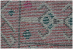 A close-up of a handmade wool rug featuring a pink, white, and teal geometric tribal pattern.
