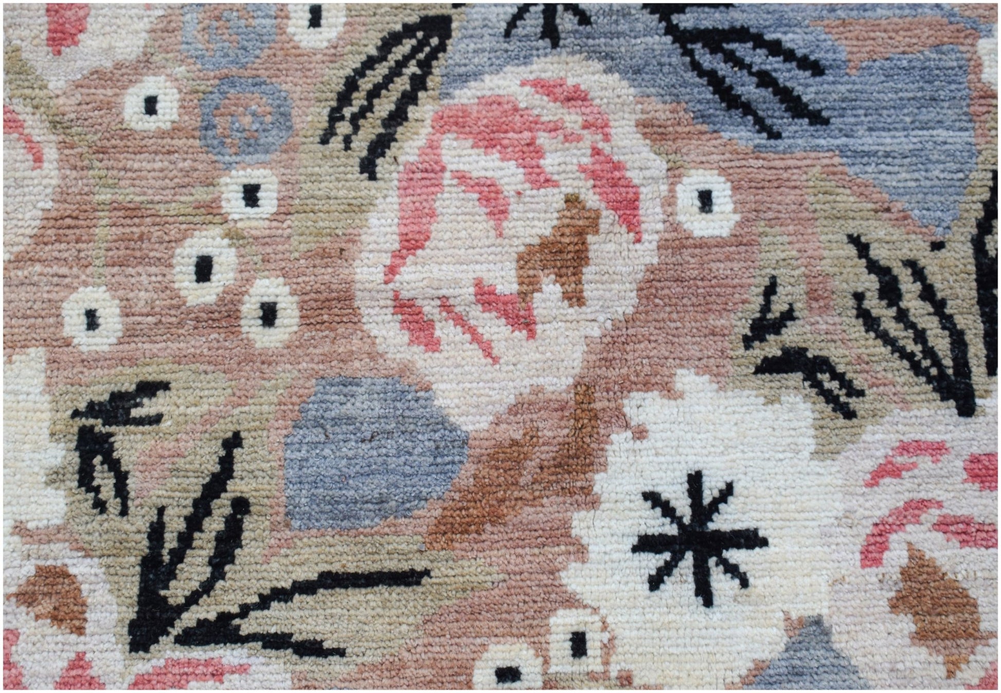 A hand-knotted wool rug featuring a floral pattern in soft pink, blue, and cream tones.