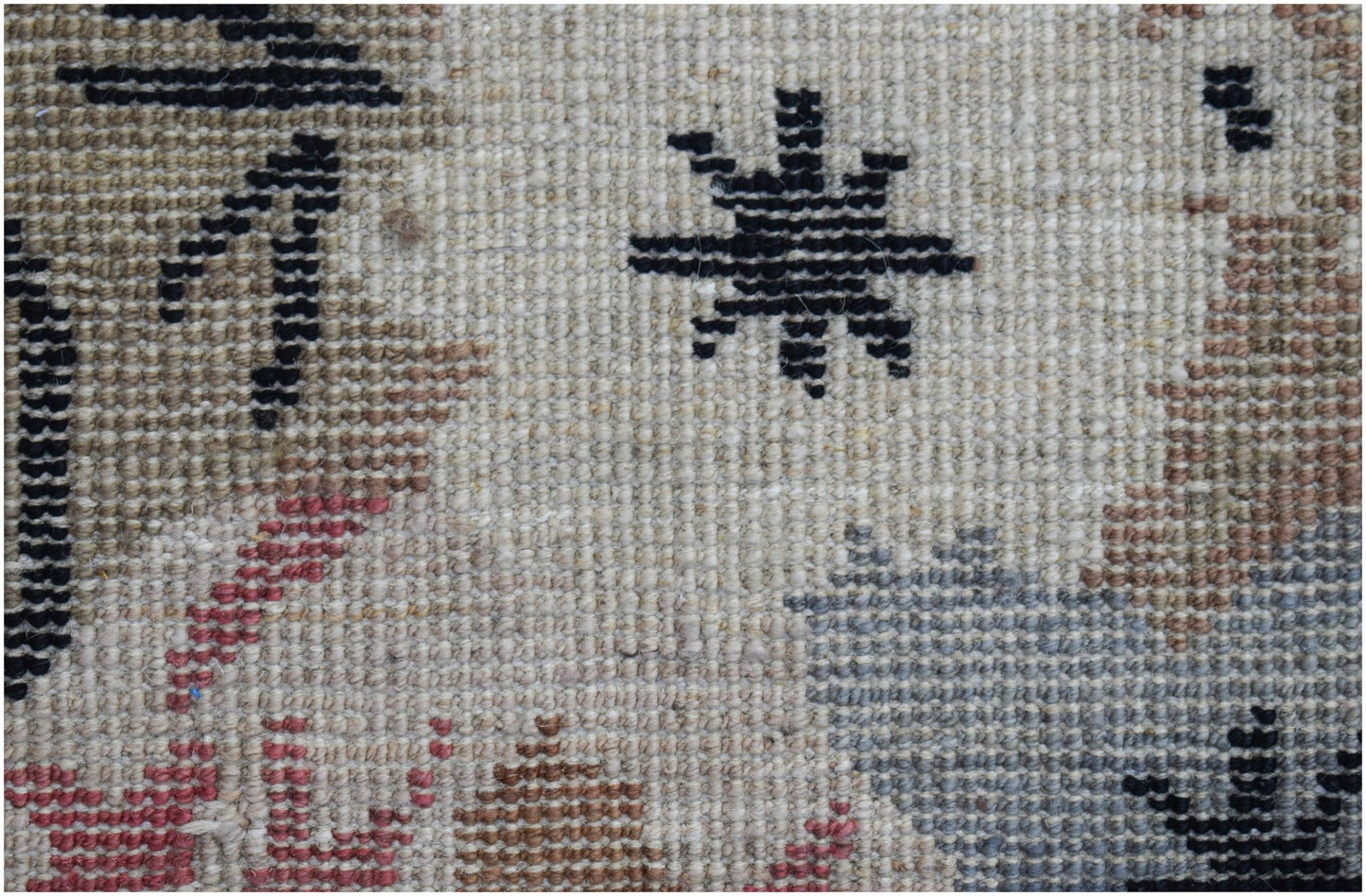 A close-up of a hand-knotted wool rug featuring a geometric star pattern on a neutral background.