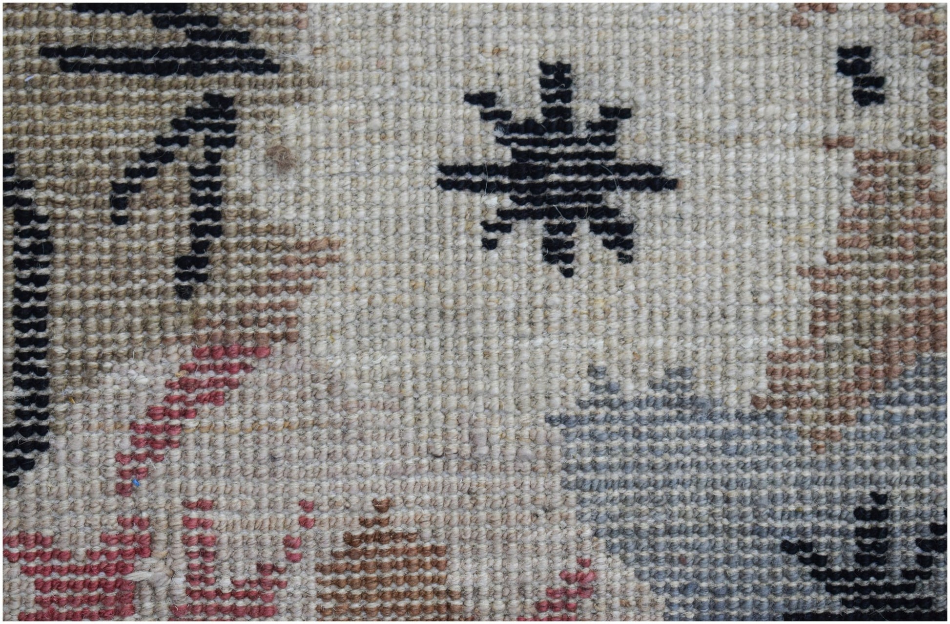 A close-up of a hand-knotted wool rug featuring a geometric star pattern on a neutral background.