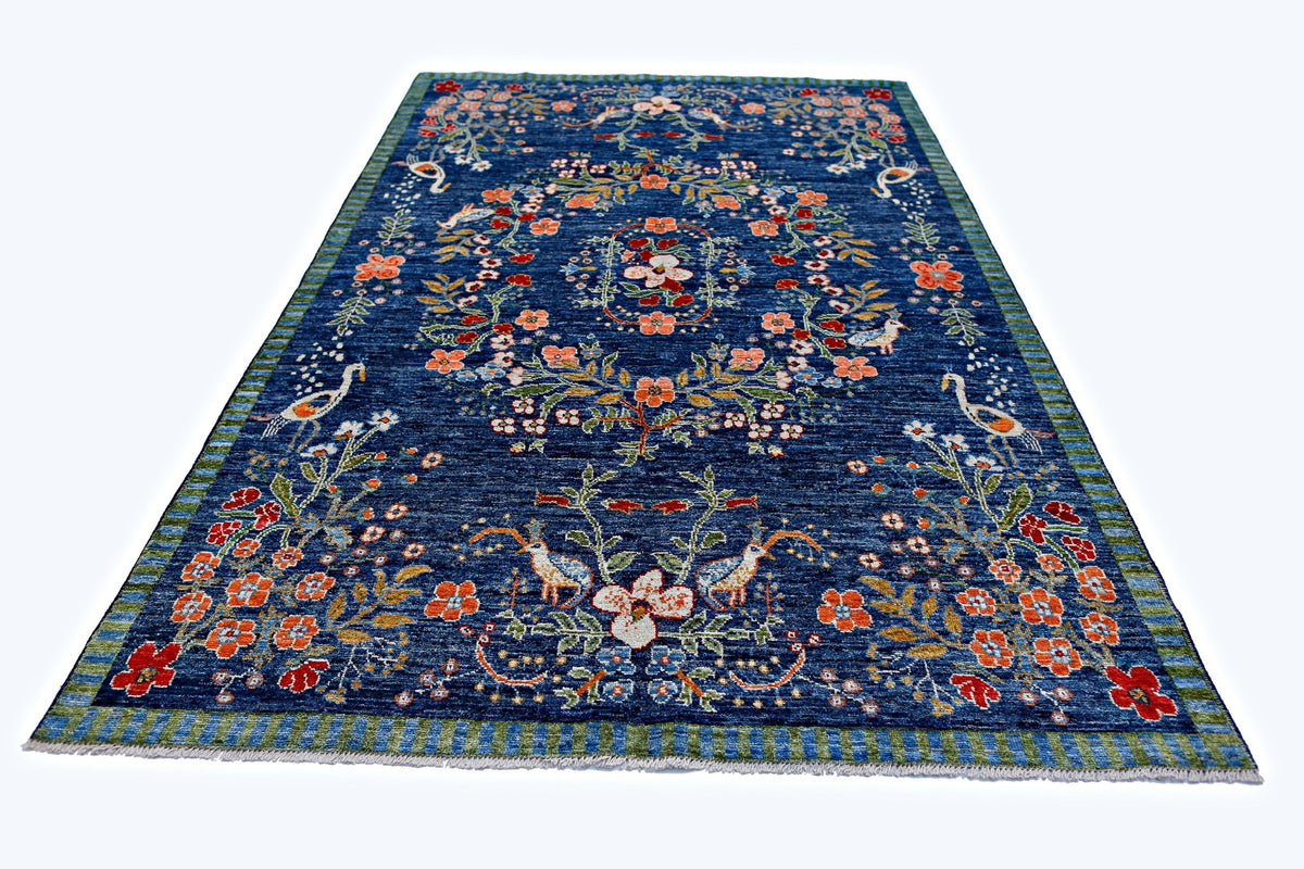 A handmade blue wool rug featuring a floral pattern with birds and a striped border.