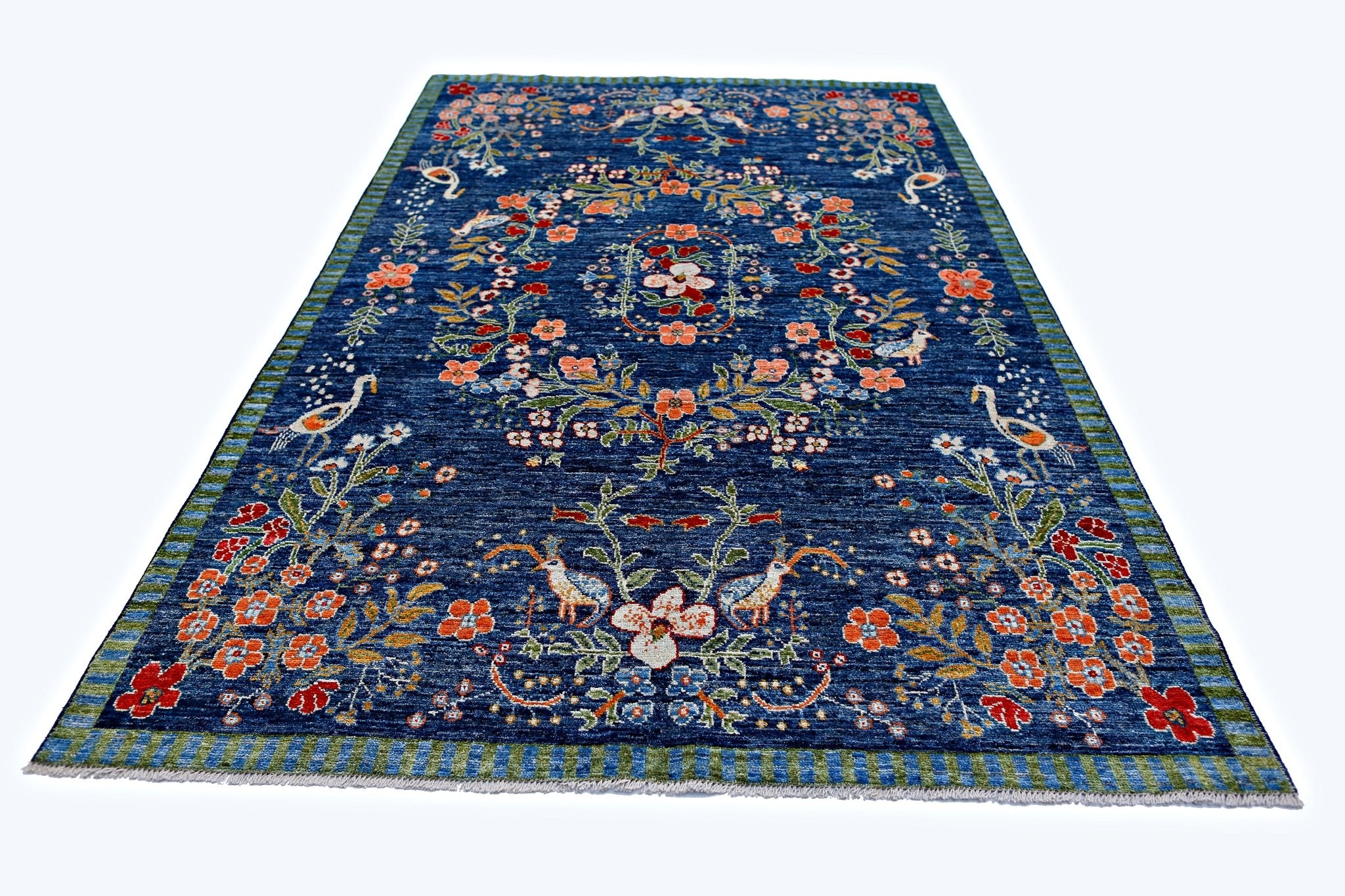 A handmade blue wool rug featuring a floral pattern with birds and a striped border.