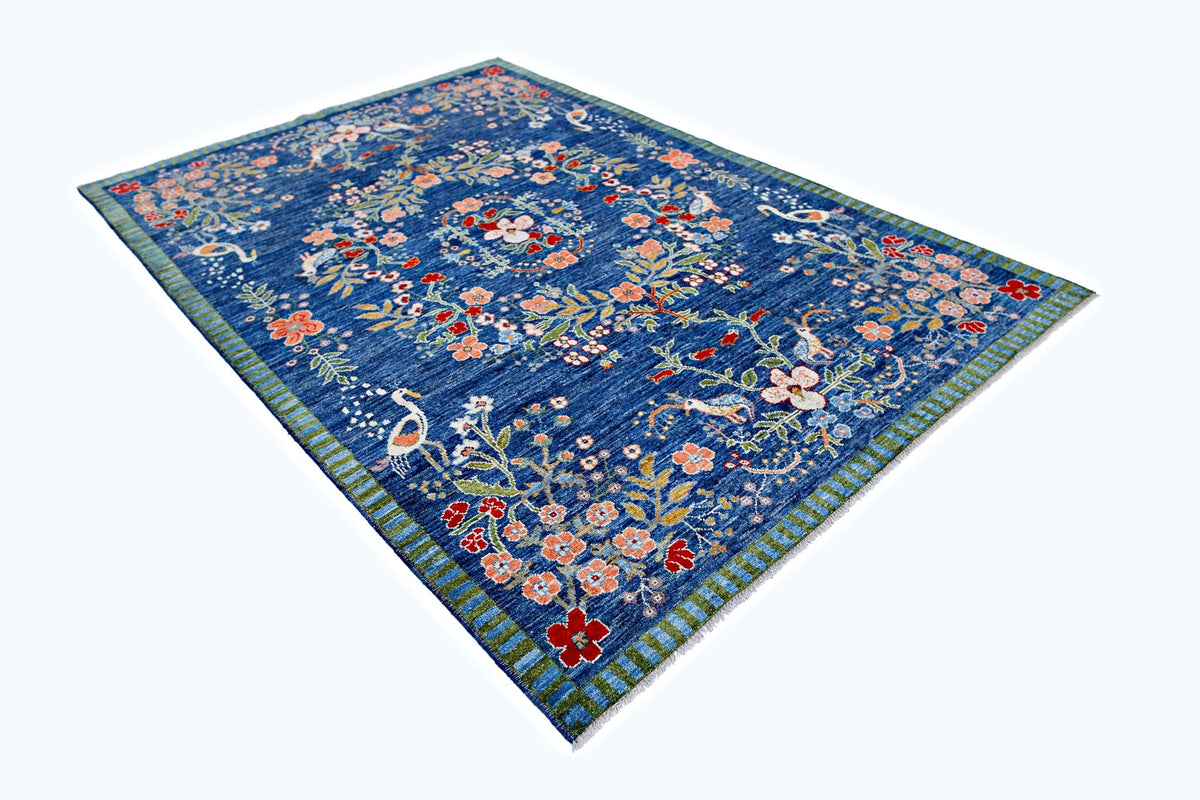 A handmade blue wool rug featuring a floral pattern with birds and a striped border.