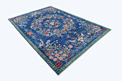 A handmade blue wool rug featuring a floral pattern with birds and a striped border.