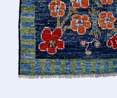 A handmade wool rug featuring a deep blue field with vibrant orange and red floral patterns.
