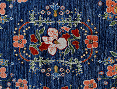 A handmade wool rug featuring a central floral medallion in white and red on a textured blue field.