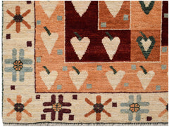 A hand-knotted wool rug featuring geometric heart motifs and floral patterns in earthy tones.
