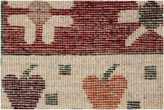 A close-up of a hand-knotted wool rug featuring geometric fruit motifs in red, orange, and green.