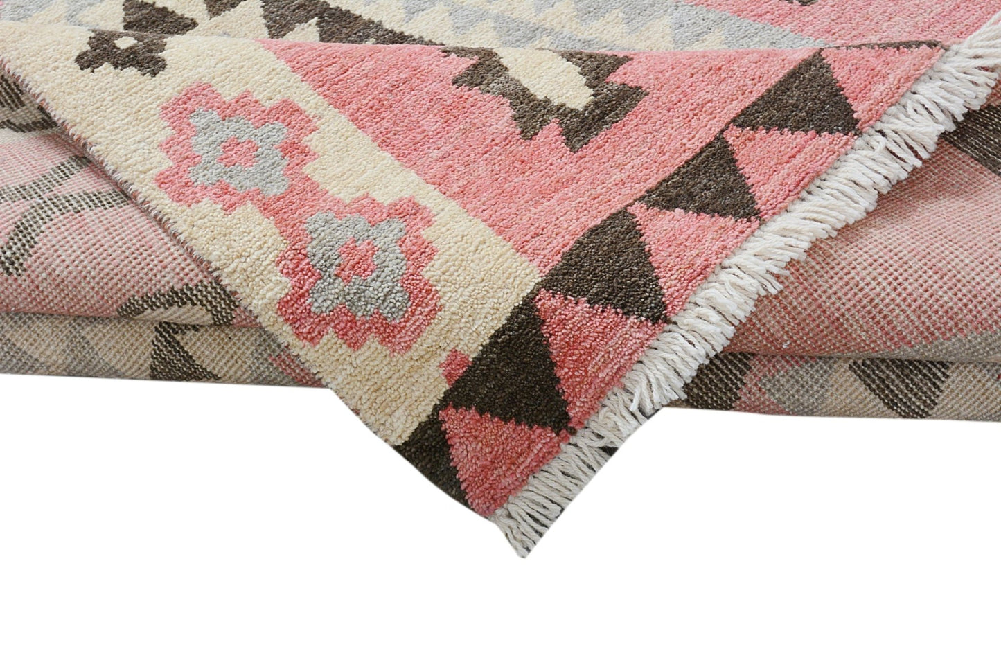 A handmade wool rug featuring a geometric tribal pattern in shades of pink, cream, and brown.