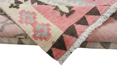 A handmade wool rug featuring a geometric tribal pattern in shades of pink, cream, and brown.