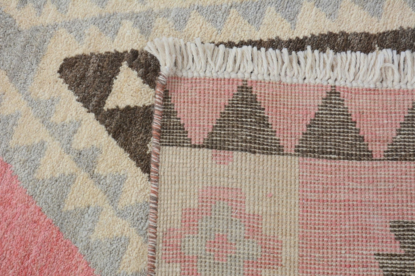 A close-up of a handmade wool rug featuring a geometric pattern in pink, brown, and cream tones.