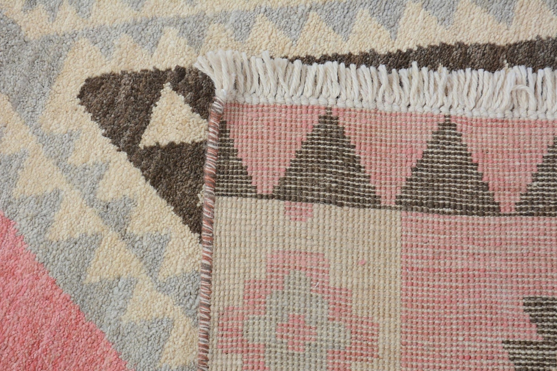 A close-up of a handmade wool rug featuring a geometric pattern in pink, brown, and cream tones.