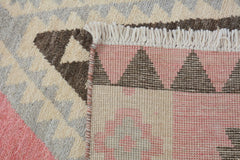 A close-up of a handmade wool rug featuring a geometric pattern in pink, brown, and cream tones.