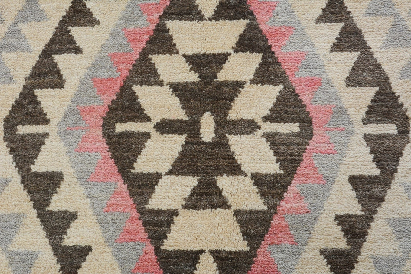 A handmade wool rug featuring a geometric tribal pattern in cream, brown, pink, and grey.