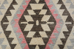 A handmade wool rug featuring a geometric tribal pattern in cream, brown, pink, and grey.