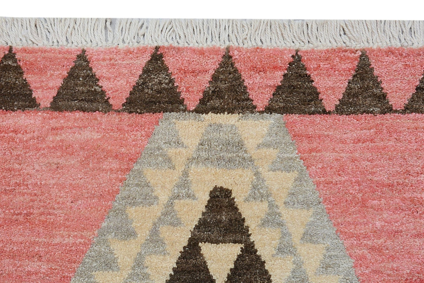 A handmade wool rug featuring a pink background with dark brown and cream geometric patterns.