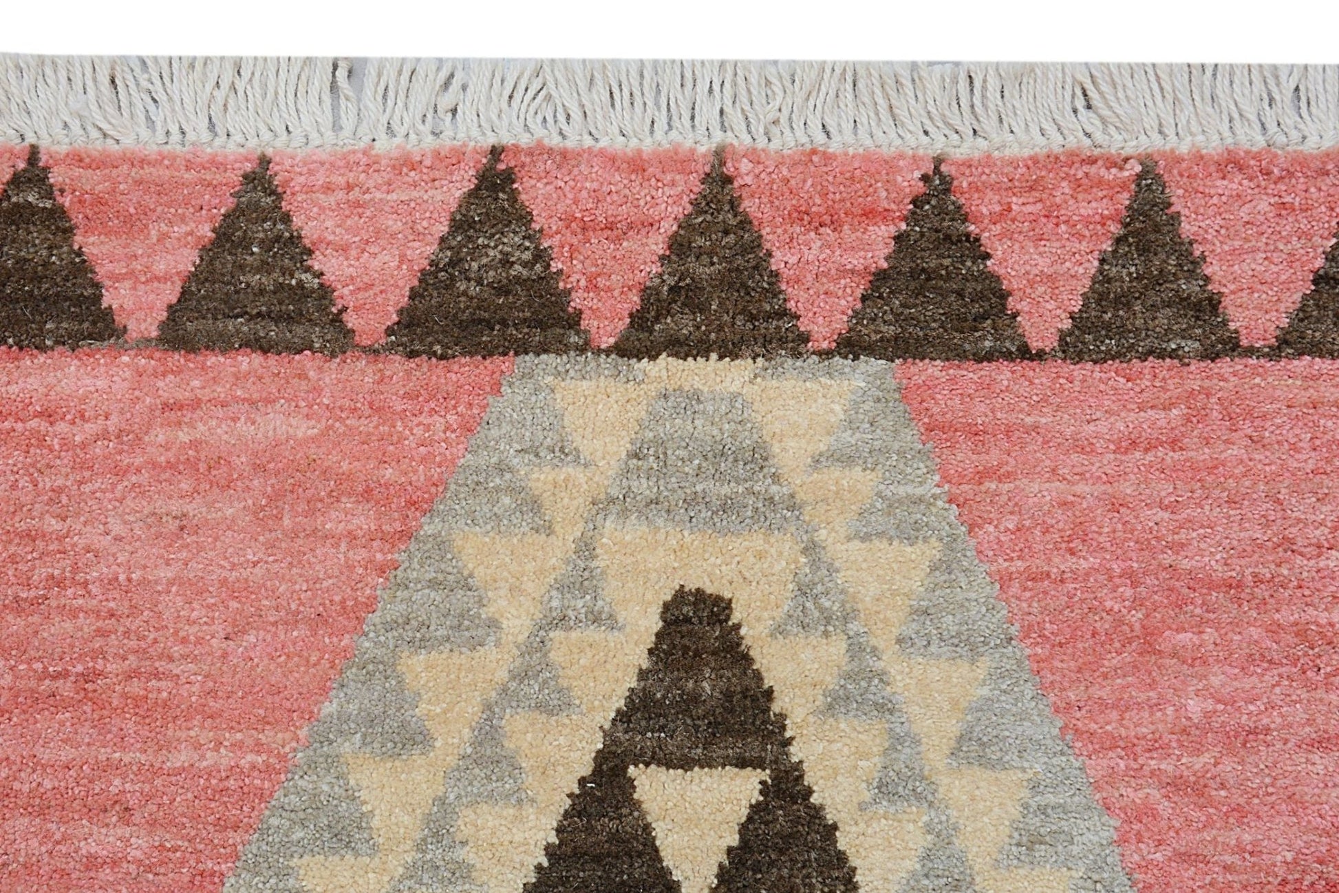 A handmade wool rug featuring a pink background with dark brown and cream geometric patterns.