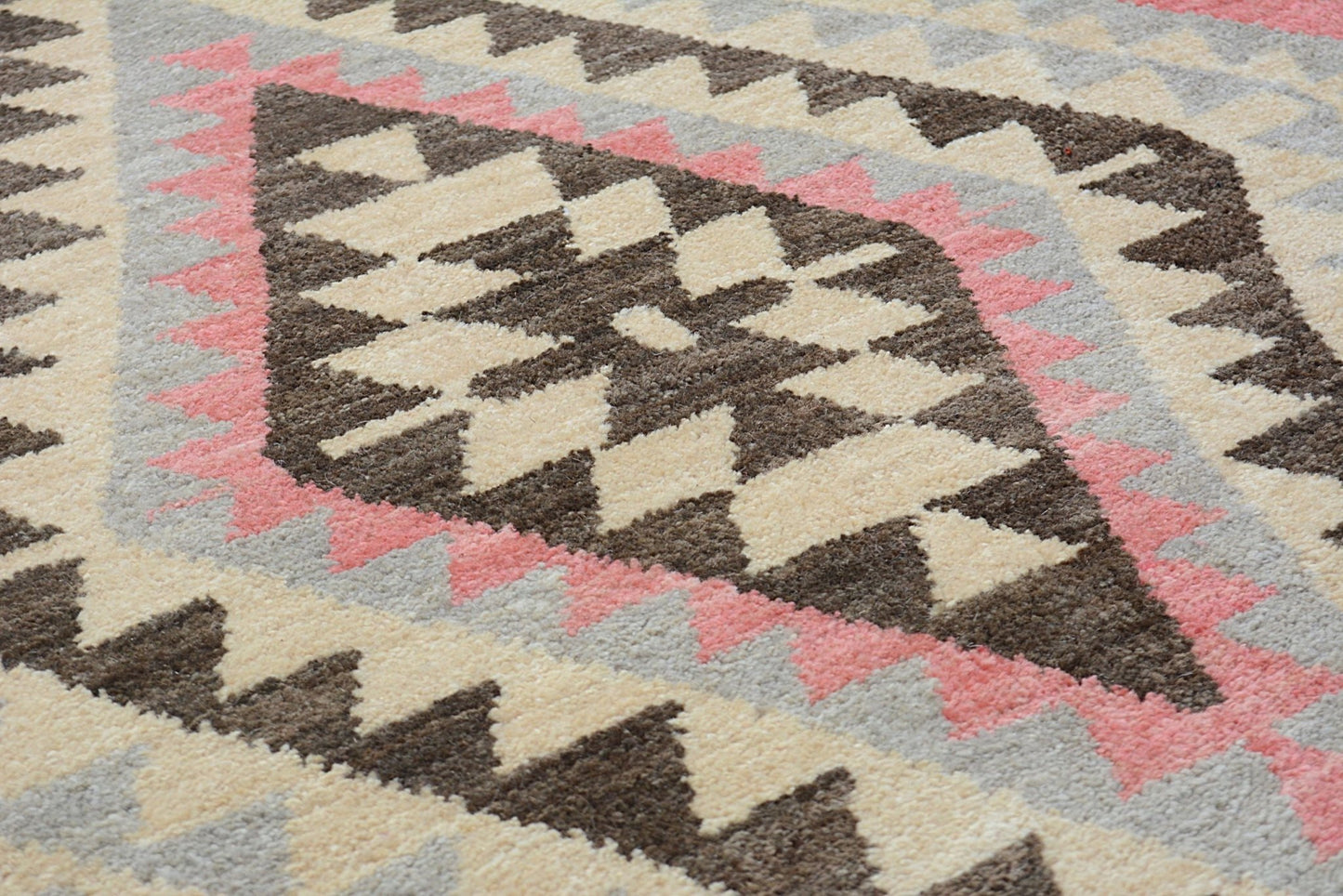 A handmade wool rug featuring a geometric diamond pattern in shades of brown, cream, and pink.