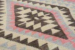 A handmade wool rug featuring a geometric diamond pattern in shades of brown, cream, and pink.