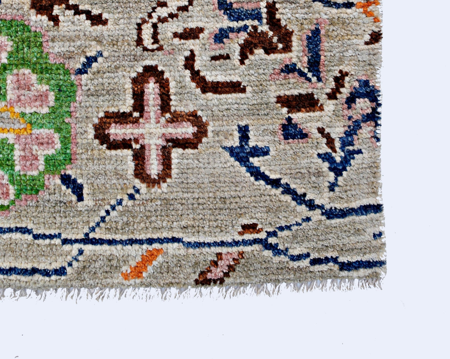 A close-up of a handmade wool rug featuring a light gray field with floral and cross motifs.