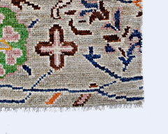 A close-up of a handmade wool rug featuring a light gray field with floral and cross motifs.