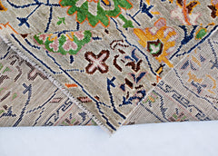 A handmade wool rug from Afghanistan featuring a colorful floral pattern on a beige background.
