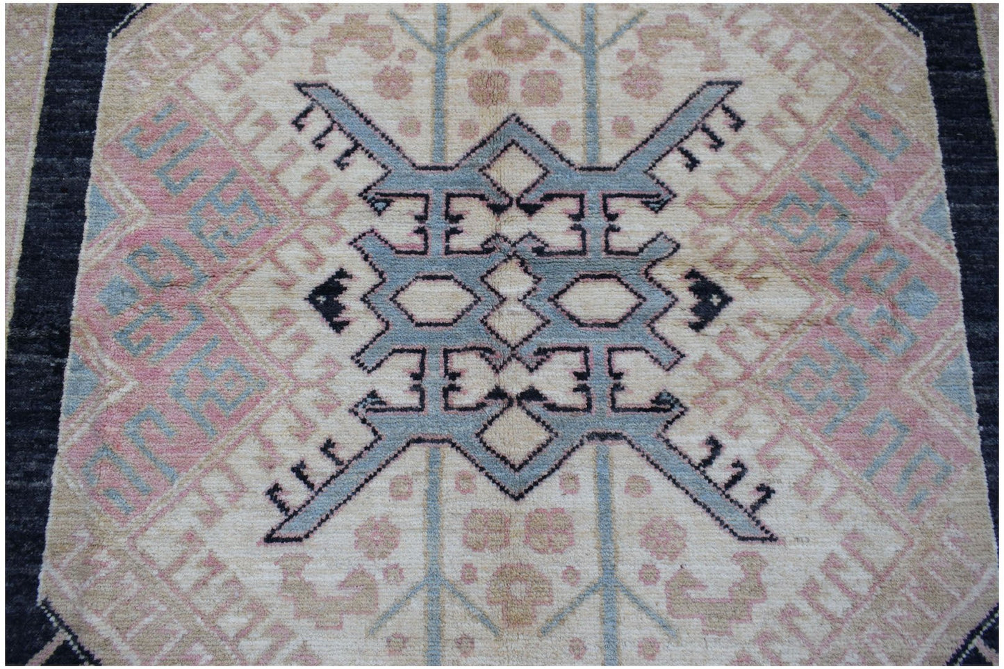 A handmade Afghan wool rug featuring a central blue geometric medallion on a cream background.