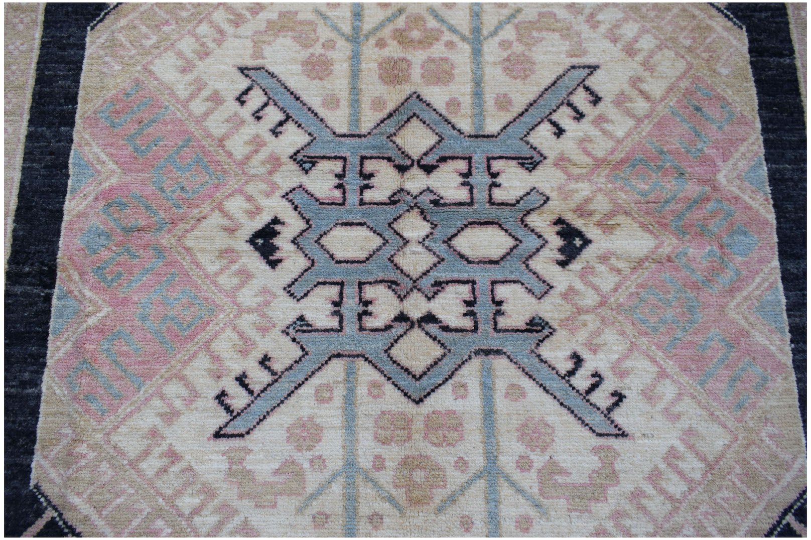 A handmade Afghan wool rug featuring a central blue geometric medallion on a cream background.